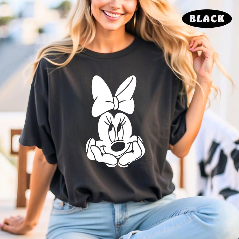 May include: Black t-shirt with a white graphic of Minnie Mouse with a bow. Minnie Mouse is smiling and has her hands clasped in front of her.