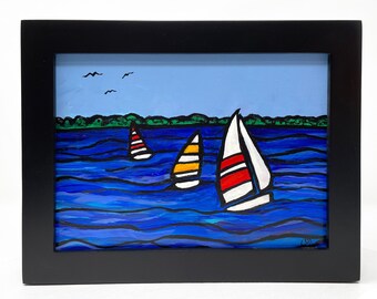 May include: A framed painting of three sailboats on a blue lake with a green shoreline in the background. The sailboats are white with red, yellow, and blue accents.
