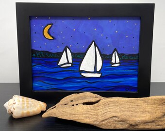 May include: A framed painting of three white sailboats on a blue body of water under a starry night sky with a crescent moon. The painting is in a black frame.