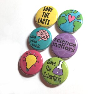 K&ouml;nnte beinhalten: Sechs bunte runde Buttons mit wissenschaftlichen Botschaften und Illustrationen. Die Buttons zeigen S&auml;tze wie "Save the Facts", "Science Matters" und "Use Your Brain".