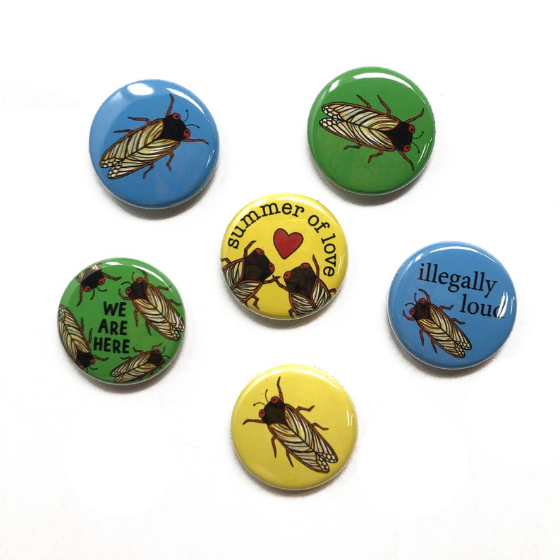 May include: Six round buttons with different designs. The buttons feature illustrations of cicadas, hearts, and text. The text on the buttons reads "We are here", "Summer of love", and "Illegally loud".