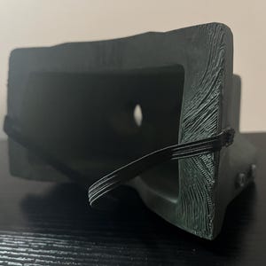 May include: A black plastic VR headset with an elastic strap. The headset has a textured surface and a small hole in the front.