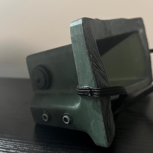 May include: A green plastic face mask with a black elastic strap. The mask has a textured surface and two small holes on the side.