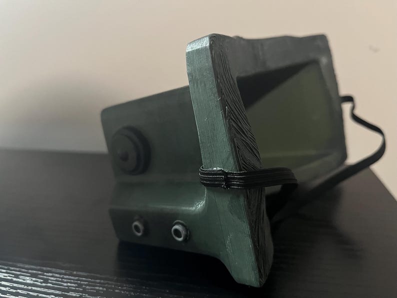 May include: A green plastic face mask with a black elastic strap. The mask has a textured surface and two small holes on the side.