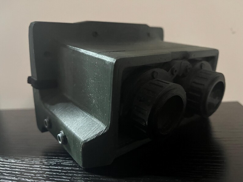 May include: A black and green plastic device with two round lenses. The device has a textured surface and appears to be a type of night vision equipment.