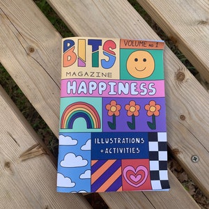 May include: A colorful magazine cover with the title "BITS MAGAZINE HAPPINESS" and the text "VOLUME no. 1". The cover features illustrations of a rainbow, flowers, clouds, a heart, and a checkerboard pattern.