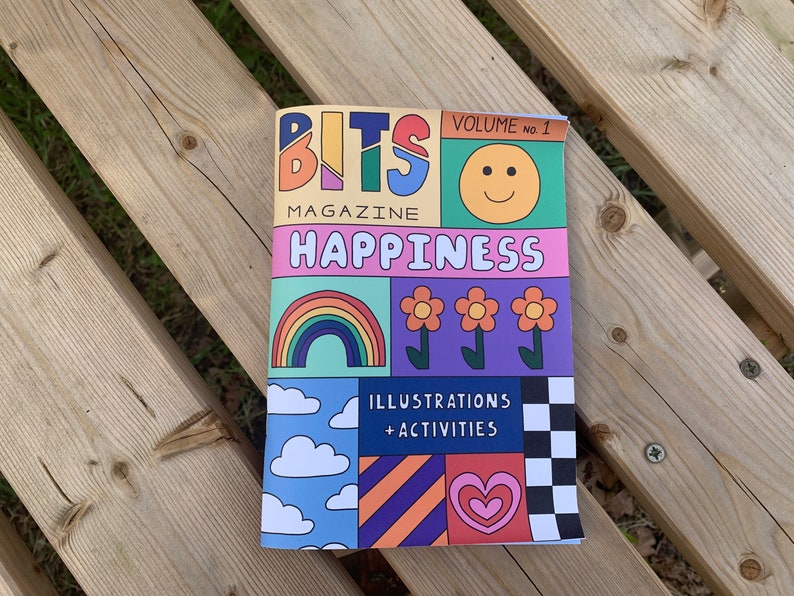 May include: A colorful magazine cover with the title "BITS MAGAZINE HAPPINESS" and the text "VOLUME no. 1". The cover features illustrations of a rainbow, flowers, clouds, a heart, and a checkerboard pattern.