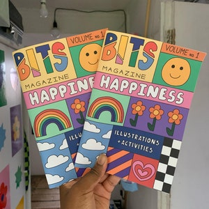 May include: Two colorful magazines titled "BITS MAGAZINE HAPPINESS" with illustrations of rainbows, clouds, hearts, and smiley faces. The magazines are volume 1.