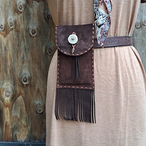 Pochette de ceinture en daim pour téléphone portable à porter avec des franges et des reflets évasés. Cousue à la main avec de la dentelle en peau de daim et ornée d'une feuille de cuivre et d'un bouton en bois de cervidé.
