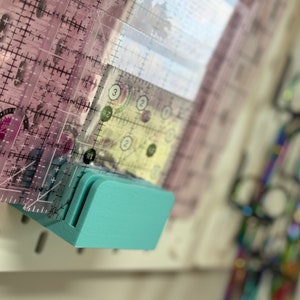 May include: A teal blue plastic organizer with a clear ruler attached to it. The ruler has a grid pattern and numbers printed on it.