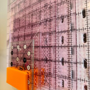 May include: A set of clear plastic rulers with black markings, including a 1-inch ruler with numbers 1, 2, and 3. The rulers are stacked on top of each other and are attached to a bright orange magnetic strip.