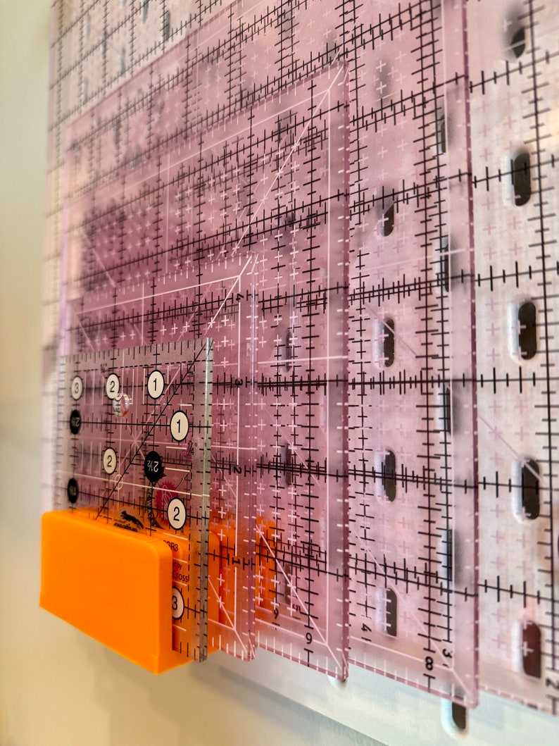 May include: A set of clear plastic rulers with black markings, including a 1-inch ruler with numbers 1, 2, and 3. The rulers are stacked on top of each other and are attached to a bright orange magnetic strip.