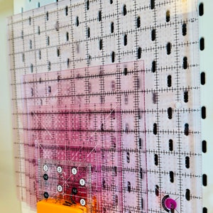 May include: A set of clear plastic quilting rulers with grid markings and inch measurements. The rulers are stacked and held in place by an orange magnetic clip.