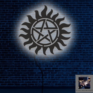 Puede incluir: Decoración de pared en blanco y negro con el símbolo icónico del programa de televisión "Supernatural". El símbolo es un pentagrama con un círculo alrededor y un diseño de rayos de sol. El símbolo está iluminado por una fuente de luz, proyectando un brillo en la pared de ladrillo detrás de él.