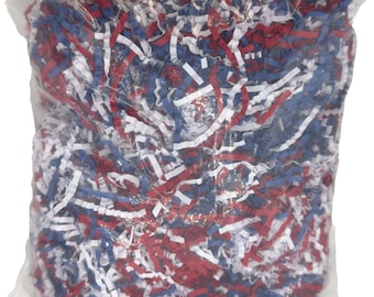 May include: A clear plastic bag filled with shredded paper in red, white, and blue. The paper is cut into thin strips, creating a textured and colorful filler. This decorative filler is suitable for gift baskets and packaging.