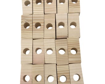 May include: A collection of small, rectangular wooden blocks with a natural wood grain finish. Each block has a circular hole drilled through the center. The blocks are arranged in a slightly overlapping pattern.