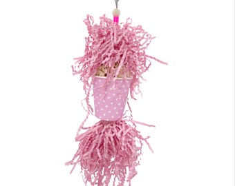 May include: A pink polka-dotted paper cup bird toy filled with pink shredded paper, suspended from a metal clip. The toy has a pink bead and a pink straw-like element. The bottom of the toy also has pink shredded paper.