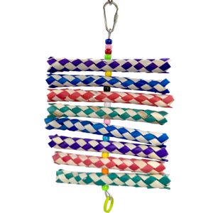 May include: A colorful woven bird toy with multiple strands of woven palm leaves in various colors, including purple, blue, green, and red. The toy is strung with colorful beads and has a metal hook for hanging.