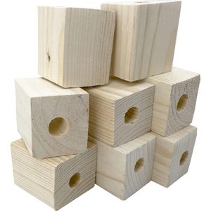 Puede incluir: Una pila de bloques de madera sin terminar, de color claro. Cada bloque tiene forma de cubo, con un agujero perforado en un lado. La veta de la madera es visible en la superficie. Los bloques están apilados en una disposición aleatoria.