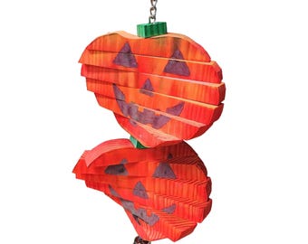 May include: A hanging Halloween decoration featuring two orange wooden jack-o'-lanterns stacked vertically. Each pumpkin has a carved face and is suspended by a silver chain. A small silver bell hangs at the bottom.