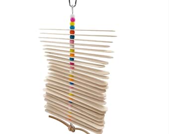 May include: A bird toy featuring a series of light-colored wooden slats suspended from a metal clip. The slats are strung together with a colorful strand of beads. A leather cord is attached at the bottom.