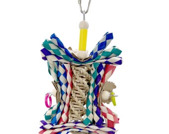 May include: A colorful bird toy with a woven center and paper accents in blue, pink, and green. The toy includes a metal clip for hanging and small plastic rings. The design is intended for bird enrichment and play.