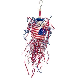 May include: A red, white, and blue bird toy with an American flag design. The toy features a cylindrical container with the flag design, filled with white objects and surrounded by red, white, and blue paper strips. A metal clip and wooden bead are at the top.