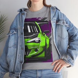 Puede incluir: Una camiseta gris con una ilustración verde y negra de un coche. El coche tiene un fondo morado y gris con rayas blancas en la parte delantera.