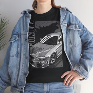 May include: A black t-shirt with a graphic of a silver Nissan Skyline GT-R R34 with the text "Godzilla" printed vertically on the left side of the image.