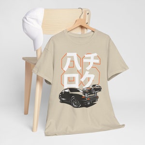 May include: A beige t-shirt with a graphic print of two black cars and the text "86" in Japanese characters. The text is in orange and white.