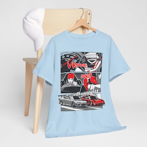 Op de afbeelding: Lichtblauw T-shirt met een stripboek-stijl grafische afbeelding van een vrouw die een auto bestuurt. De afbeelding bevat de woorden "VROOOOM!" en "BANG!"