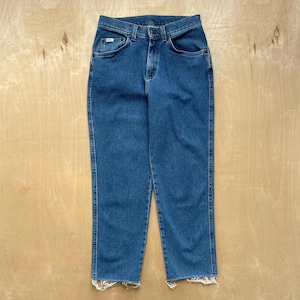 May include: Blue denim jeans with a classic five-pocket design. The jeans have a straight leg cut and a raw, frayed hem. The Lee logo is visible on the front pocket. The jeans are displayed on a light wood surface.