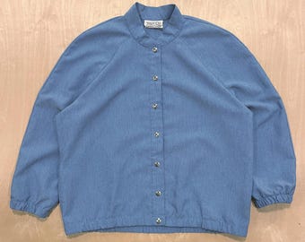 May include: A light blue jacket with a stand-up collar and long sleeves. The jacket has a button-up front with silver-colored buttons and a small label at the collar. The jacket is made of a lightweight fabric and has a casual style.