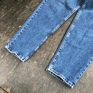 Op de afbeelding: Close-up van een blauwe spijkerbroek. De jeans heeft een klassieke rechte pijp met zichtbare stiksels langs de naden en zomen. De denim heeft een medium wassing en de afbeelding toont het onderste deel van de broek.