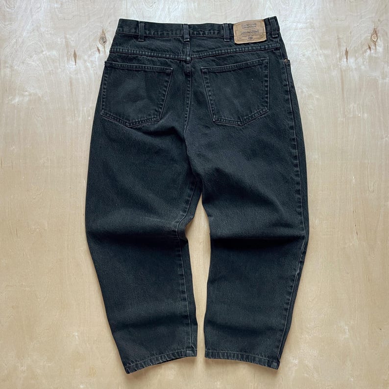 Peut inclure: Un jean en denim noir avec une taille haute et une conception classique &agrave; cinq poches. Le jean a une jambe droite et un patch en cuir sur la ceinture arri&egrave;re. Le denim semble &ecirc;tre pr&eacute;-usag&eacute;.
