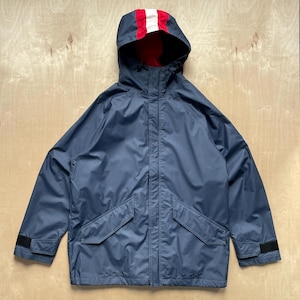 May include: A navy blue hooded jacket with a red and white striped hood lining. The jacket has two front pockets, a zipper closure, and adjustable cuffs. The jacket is made of a water-resistant material.