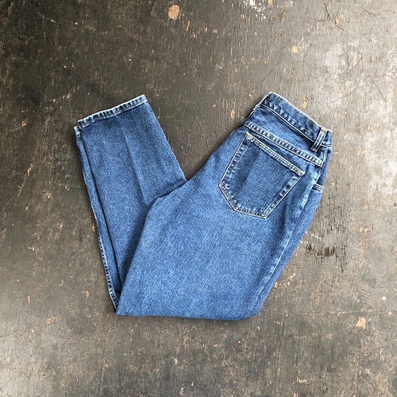 Op de afbeelding: Een paar blauwe denim jeans, opgevouwen. De jeans hebben een klassiek vijf-zakken ontwerp, een knoop- en ritssluiting en een rechte pijp. De denim heeft een medium wassing met subtiele vervaging.