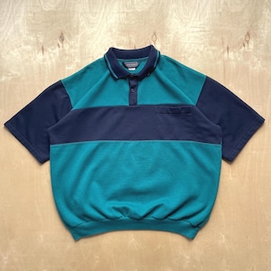 Pode incluir: Uma camisa polo em blocos de cores verde-azulado, azul marinho e verde-azulado escuro. A camisa tem mangas curtas, gola e um bolso no peito. A camisa tem uma carcela abotoada.