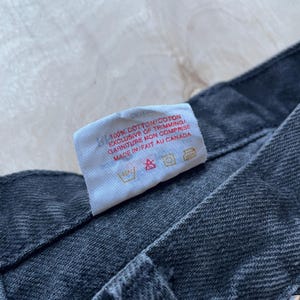 Peut inclure: Gros plan sur une &eacute;tiquette blanche avec du texte noir indiquant "100% COTTON/COTON EXCLUSIVE OF TRIMMING/ GARNITURE MON COMPRISE MADE IN/FAIT AU CANADA". L'&eacute;tiquette est sur un jean en denim gris fonc&eacute;.