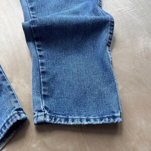 May include: Close-up of light blue denim jeans. The jeans are folded, showing the hem and the fabric's texture. The denim has a classic, slightly faded look, with visible stitching details.
