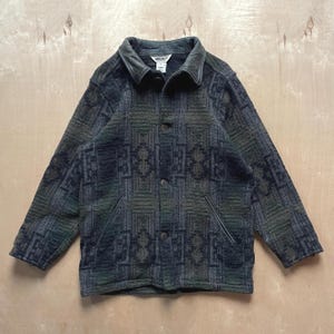 Peut inclure: Veste boutonnée à motifs géométriques verts, gris et noirs. Le col est en cuir et il y a deux poches avant. La veste est de taille moyenne. Les mesures sont en centimètres.