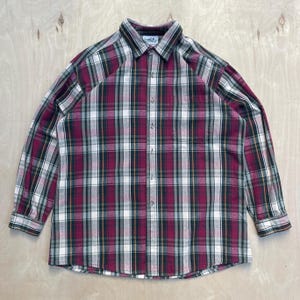 May include: A long-sleeved plaid shirt in a classic pattern. The shirt features a burgundy, green, white, and gold plaid design. It has a button-down front, a collar, and a single chest pocket. The shirt is made of a soft, woven fabric.