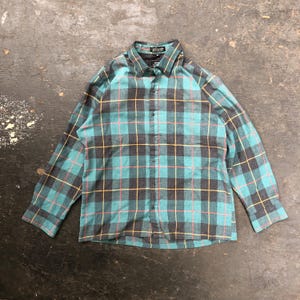 以下が含まれることがあります： ターコイズ、ブラック、イエロー、ピンクの色の長袖のチェックシャツ。シャツはボタンダウンカラーとボタンフロントです。