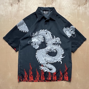 May include: Black button-up short-sleeve shirt with a large white and gray dragon design on the front and sleeves. Red flames are printed along the bottom hem. The shirt has a classic collar.