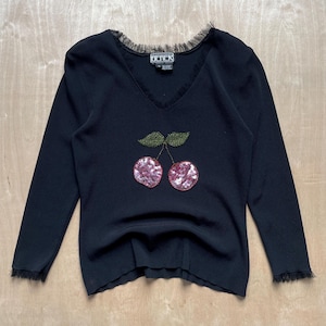 Könnte beinhalten: Schwarzer Langarm-Pullover mit V-Ausschnitt und einem Pailletten-Kirsch-Design. Der Pullover hat einen Spitzenbesatz am Ausschnitt und an den Ärmeln.