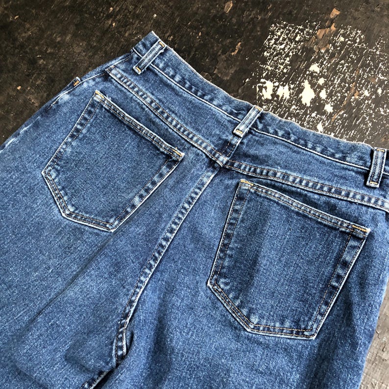 Op de afbeelding: Close-up van de achterkant van een blauwe spijkerbroek. De jeans heeft twee achterzakken, riemlussen en een klassiek ontwerp. De denim heeft een medium wassing en de stiksels zijn zichtbaar. De jeans is waarschijnlijk vintage of pre-owned.