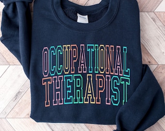 May include: A navy blue crewneck sweatshirt featuring the text OCCUPATIONAL THERAPIST printed in a collegiate font. The letters are outlined in a vibrant gradient of pink, orange, yellow, and teal colors, creating a bold and colorful graphic design.