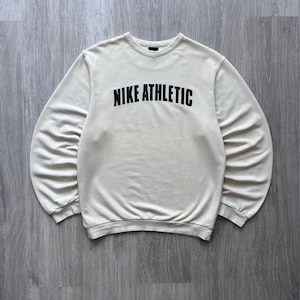 Puede incluir: Sudadera color crema con la inscripci&oacute;n "NIKE ATHLETIC" en letras negras en el pecho. La parte superior de manga larga tiene cuello redondo y pu&ntilde;os acanalados. La sudadera es de material suave.