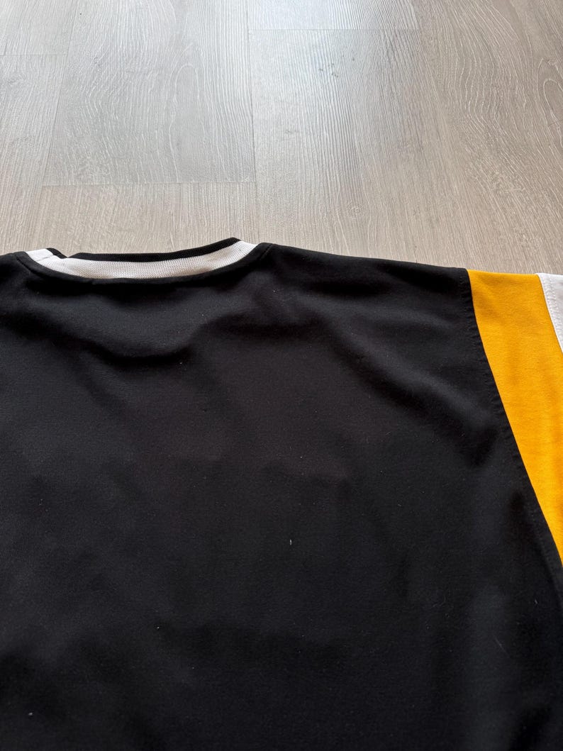 Puede incluir: Sudadera negra de cuello redondo con cuello a rayas blancas y negras. La manga derecha es amarilla y gris. La sudadera est&aacute; hecha de un material suave.