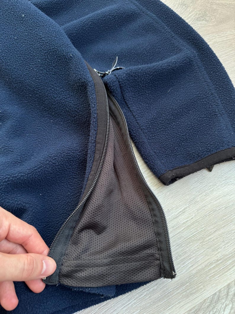 May include: Navy blue fleece jacket with a full-length zipper. The jacket has a black zipper and trim. The interior lining is a dark gray mesh material. The fleece material is soft and textured.